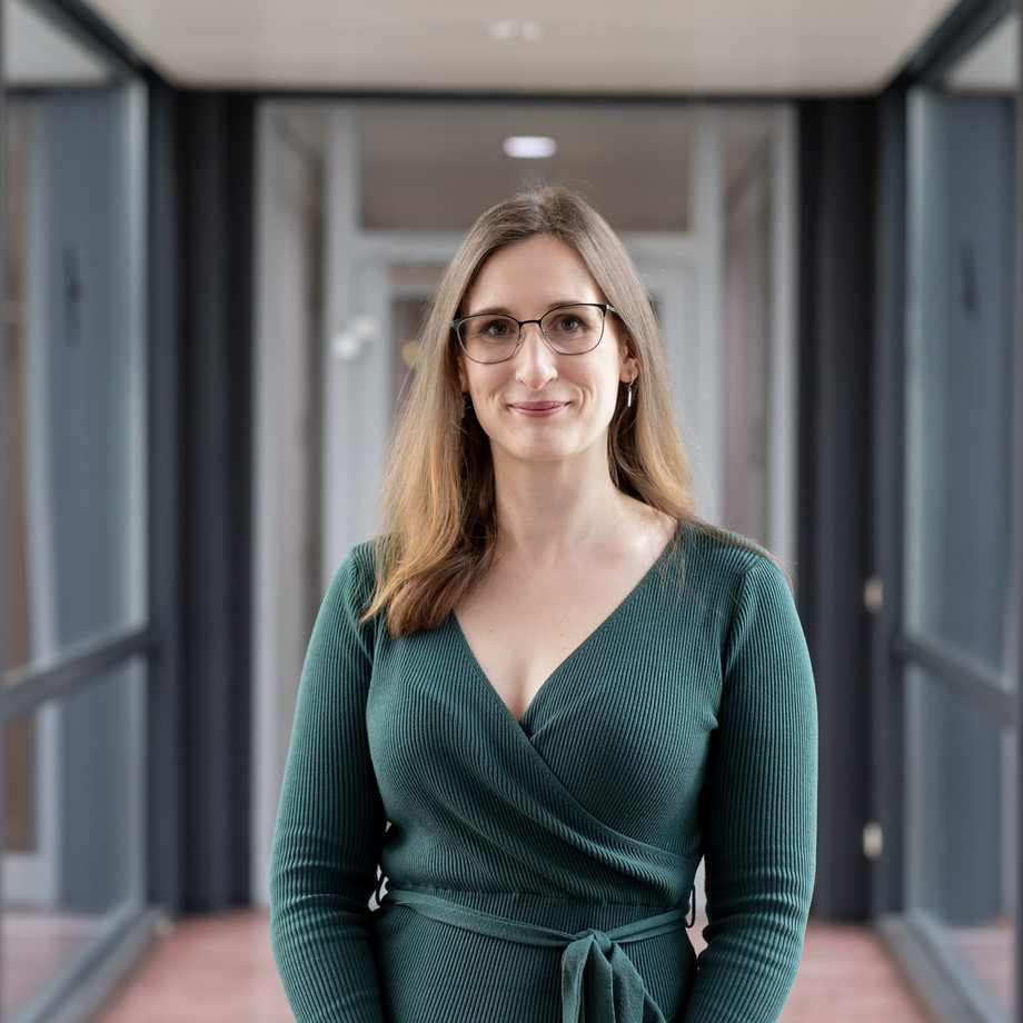 Eine Frau mit Brille steht in einem modernen Raum mit Glaswänden.