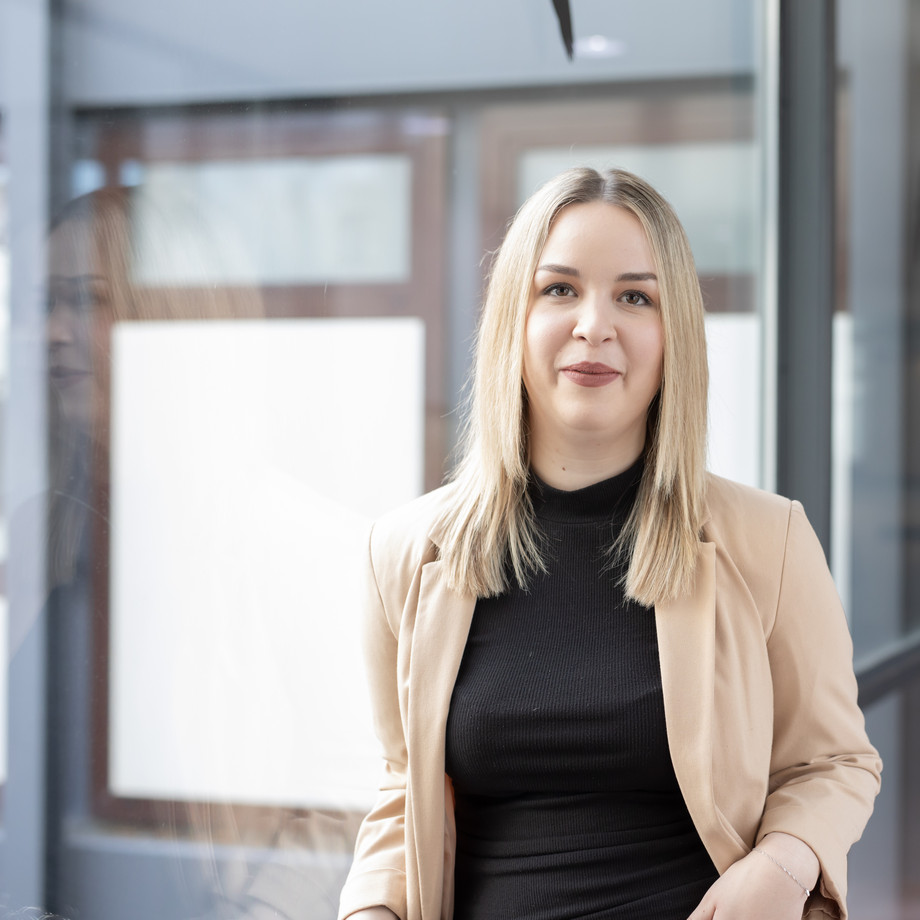 Katharina Kolb steht vor einem Gebäude mit Glasfenstern.